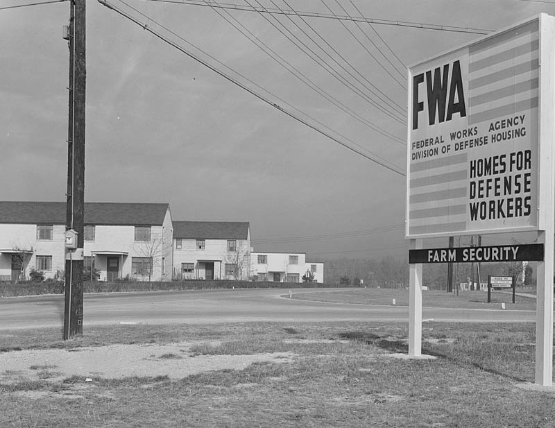 Photograph of a Greenbelt neighborhood with a sign reading "Federal Works Agency division of defense housing, homes for defense workers, farm security."