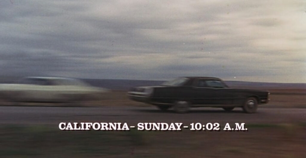 Film still of Kowalski's white Dodge Challenger crossing paths with a black Ford LTE heading in the opposite direction, caption of "California - Sunday - 10:02 A.M."