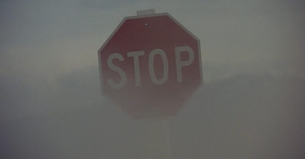 Film still zoomed in on the face of a stop sign with dust blowing past it.